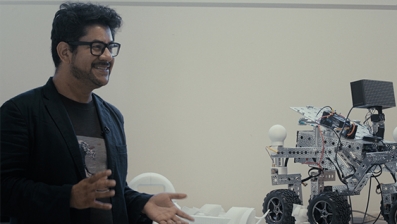 Dr Eduardo Benitez Sandoval beside a four-wheeled robot used in the Creative Robotics LabE